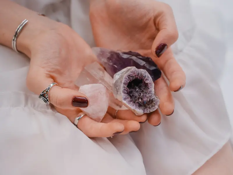 Close-up of a woman holding a collection of crystals, including clear quartz, amethyst, and rose quartz.