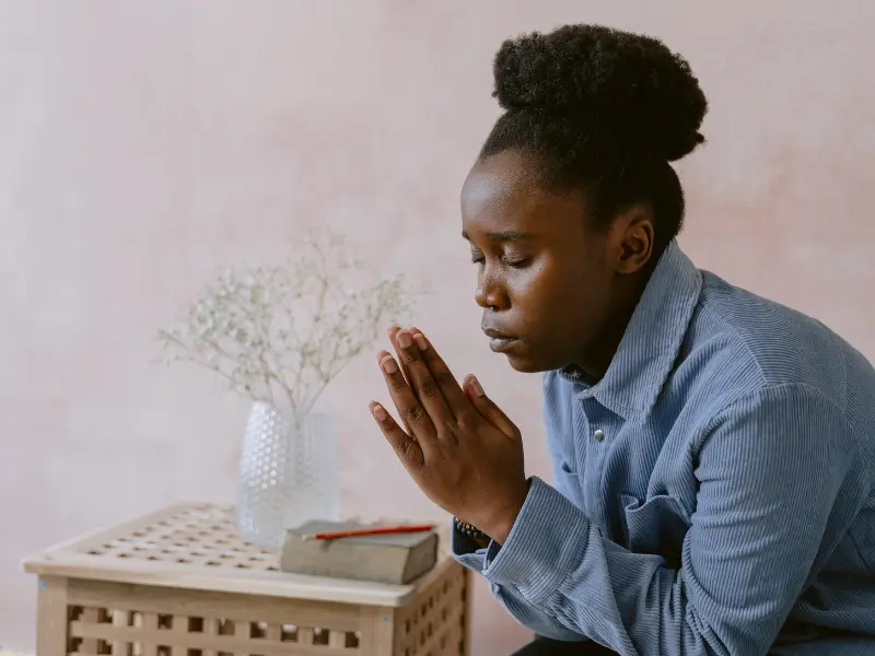 A profile of a woman with her eyes closed and hands in prayer. 