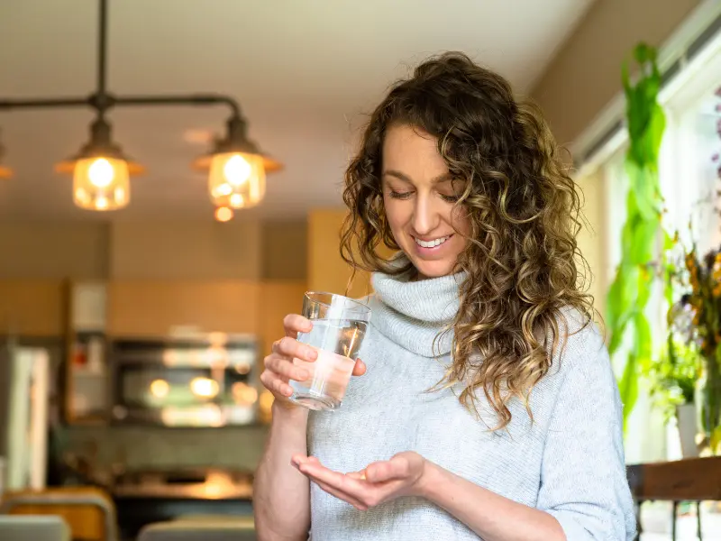 Woman smiling while holding a cup of water and supplements.