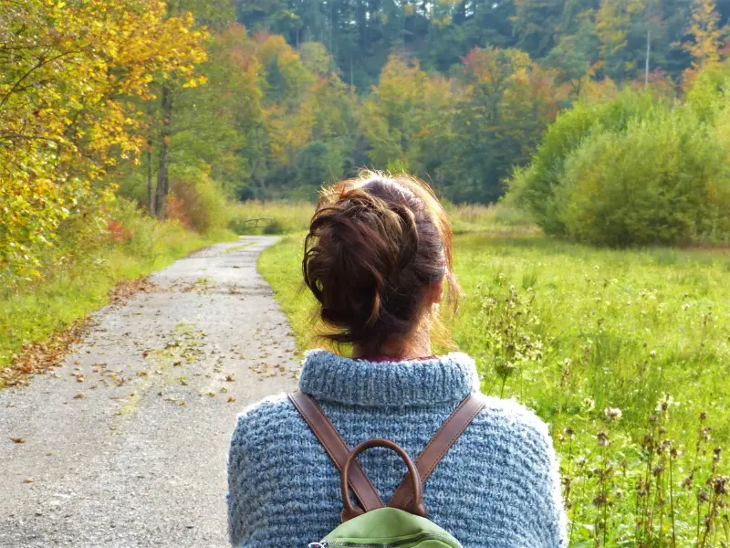 Woman walking on a scenic autumn trail, surrounded by colorful fall foliage.