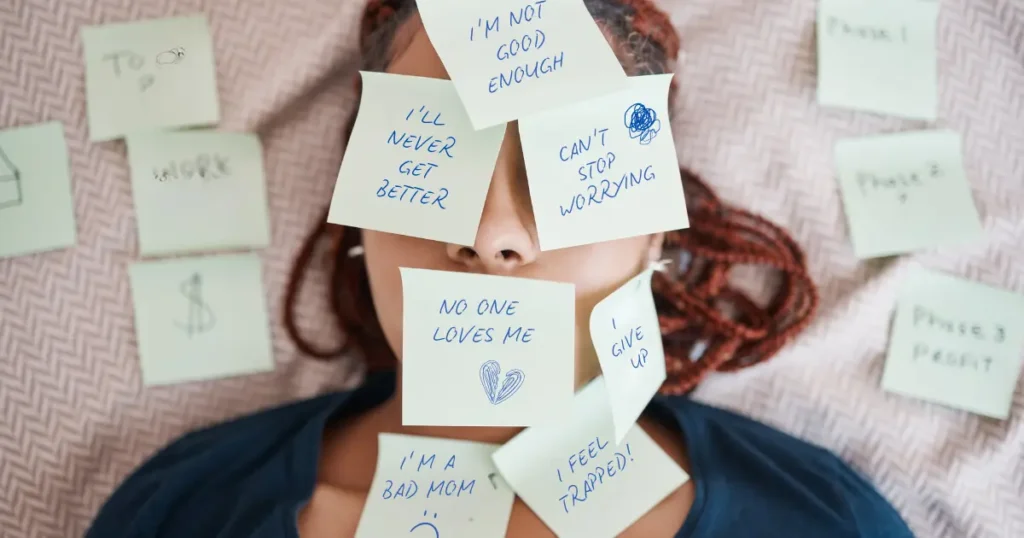 A person’s face is covered with sticky notes, each displaying a different negative thought, such as "I'm not good enough," "I'll never get better," and "No one loves me.