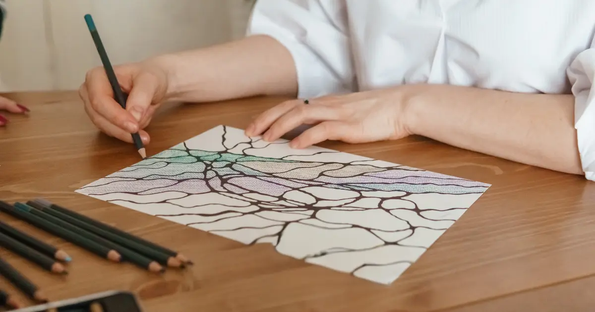 A woman creating abstract art with colored pencils on a piece of paper at a desk.