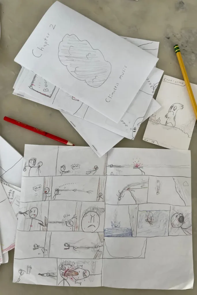 A collection of hand-drawn comic strips and sketches on folded paper, with a red and yellow pencil placed nearby.