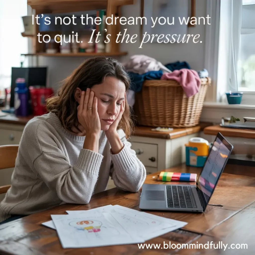 An overwhelmed mom sits at a cluttered kitchen table holding her head, with the quote, “It’s not the dream you want to quit. It’s the pressure,” offering emotional support and a mindset shift toward resilience.
