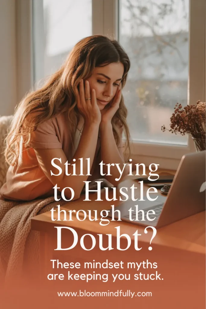 A woman sits thoughtfully in front of a laptop, with text that reads “Still trying to Hustle through the Doubt? These mindset myths are keeping you stuck.” Highlights entrepreneur mindset myths affecting mom entrepreneurs.