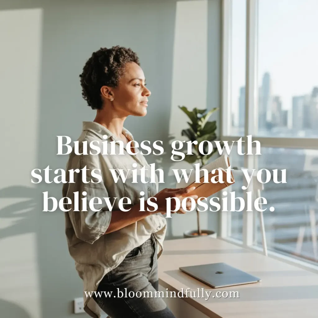 Calm woman entrepreneur holding journal by window, quote overlay says: “Business growth starts with what you believe is possible.”