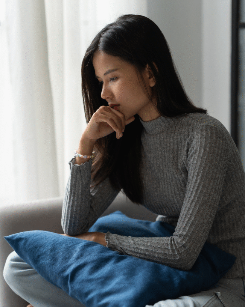 asian woman overthinking sitting on the couch