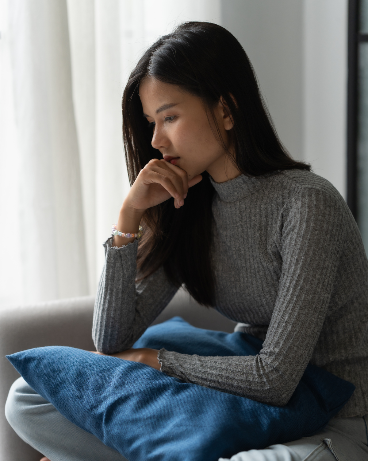 asian woman overthinking sitting on the couch